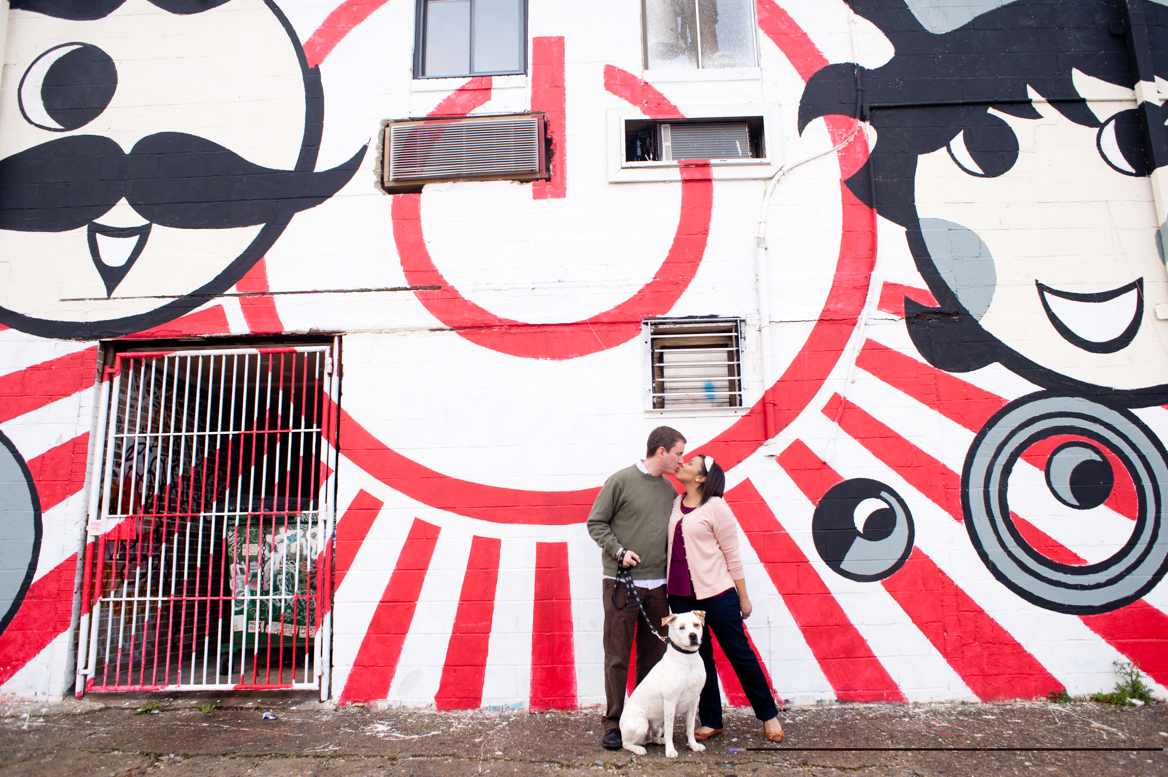 erik & mallorie kissing with dog Rock, in front of Boh & Utz mural in Baltimore