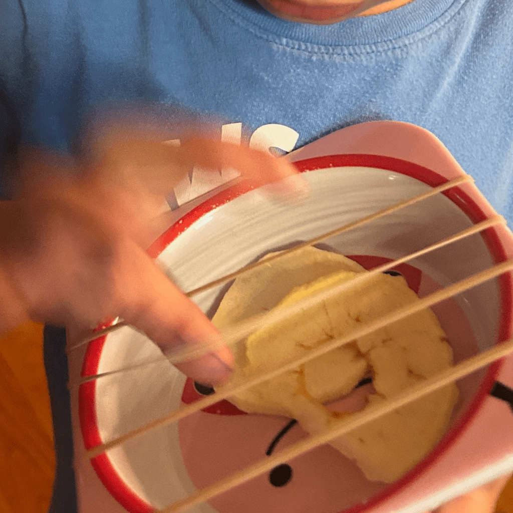 pic of son playing rubber-band guitar he made with his bowl filled with dried apple slices